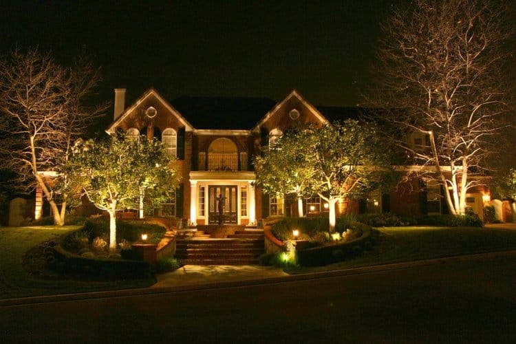 landscape lighting illuminates the house and its surrounding trees and bushes.